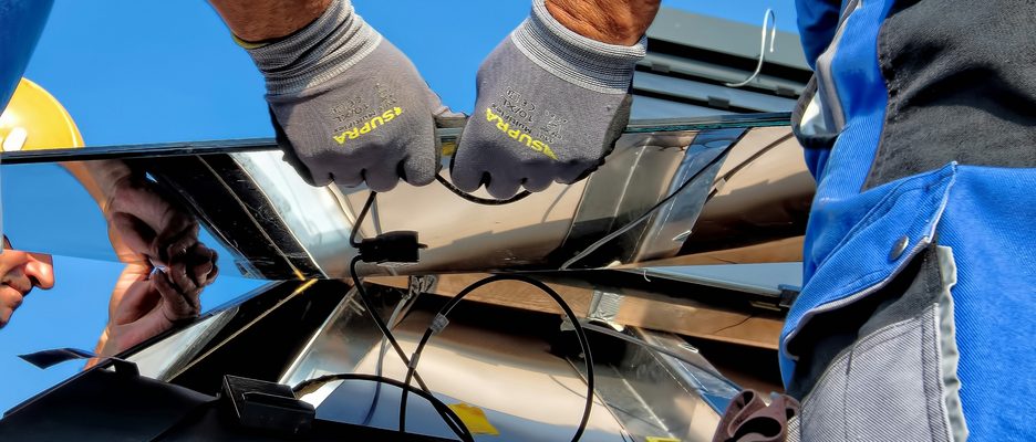 Gloved hands connecting the wiring beneath a solar panel during installation