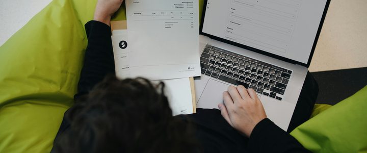 A person reviewing a printed invoice next to an open laptop